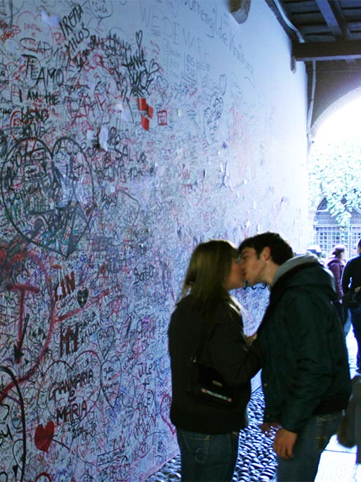 A boy and a girl kiss in front of the graffiti covered wall in the entrance of Juliet's house.