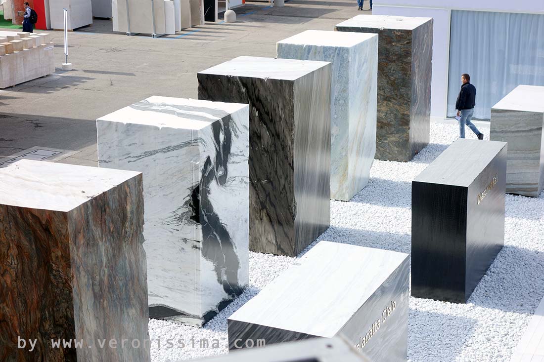 un uomo cammina tra gli immensi blocchi di marmo grezzo esposti sul piazzale della fiera