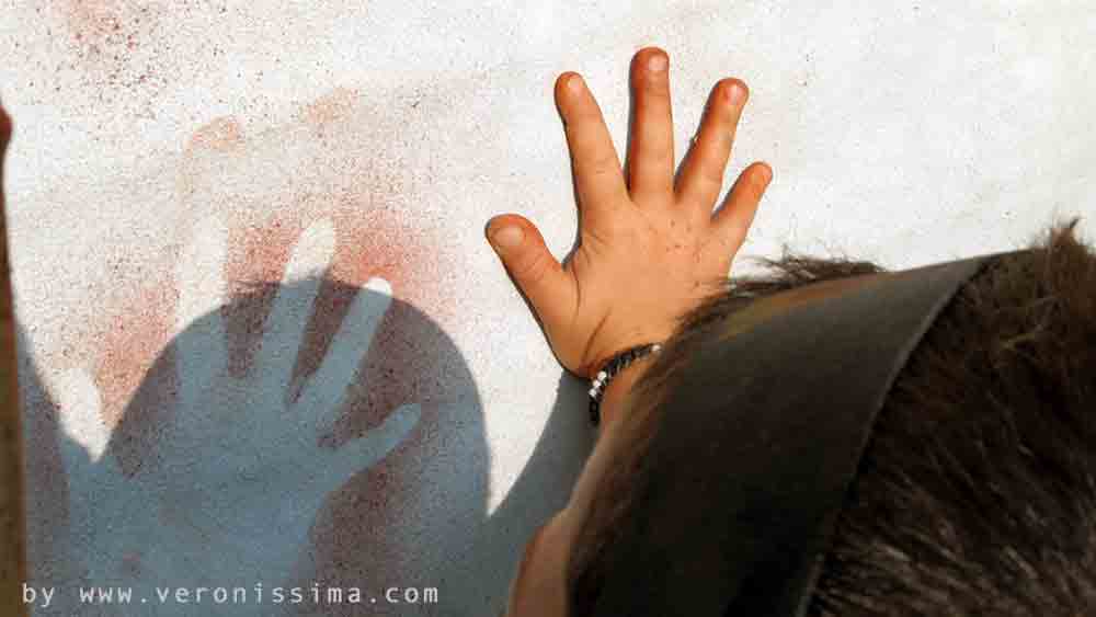 Un bambino dipinge con ocra a spruzzo la sagoma della sua mano
