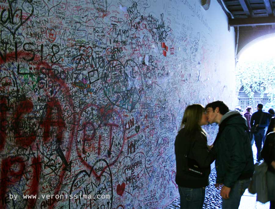 una giovane coppia si bacia davanti al muro con le scritte degli innamorati alla casa di Giulietta a Verona