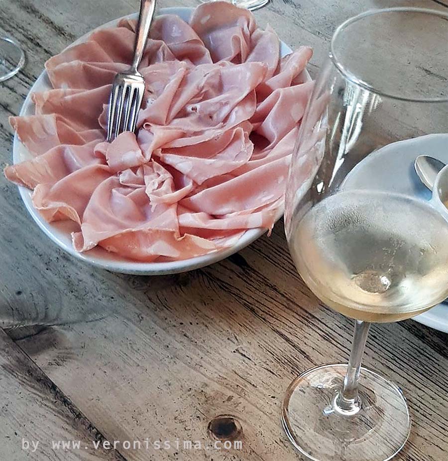 A glass of Durello with a platter of mortadella